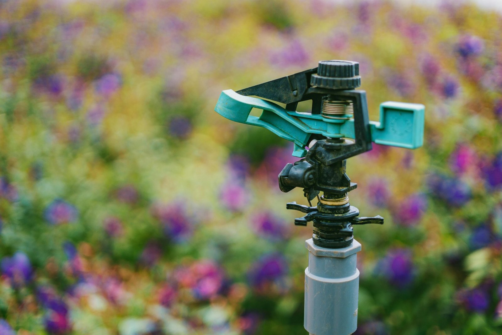Detailed close-up of a garden sprinkler with colorful flowers in soft focus background.